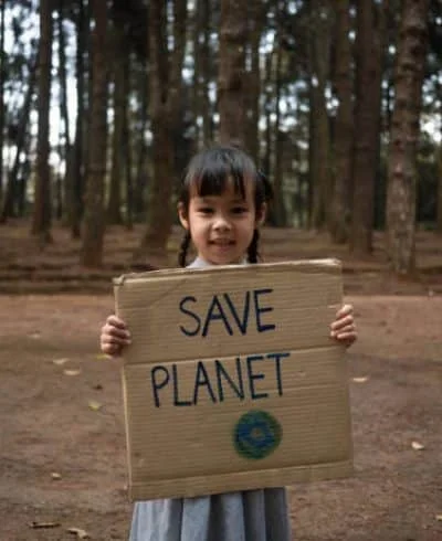 A small girl holds a cartoon paper that contains the text save planet